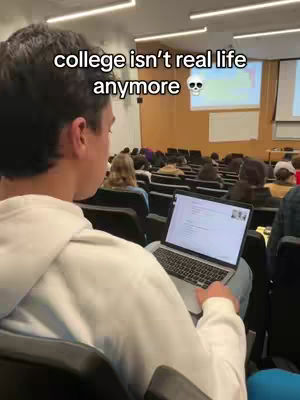 A person is seated, viewed from behind, in a lecture hall, facing a laptop on a desk. The text overlayed on the top states: college isn't real life anymore