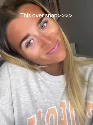 A close-up shot of a woman with blonde hair, fair skin, and light blue eyes. She is wearing a light gray sweatshirt. The text overlay reads 'This over snap>>>'.