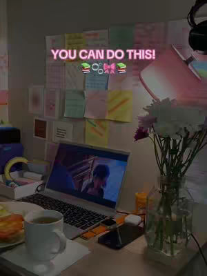 A well-lit desk scene with a laptop displaying an image of a person, a white mug, a smartphone, and a glass vase with flowers. Sticky notes are on the wall behind the laptop. The words "YOU CAN DO THIS!" are written in a pink, glowing font across the image.