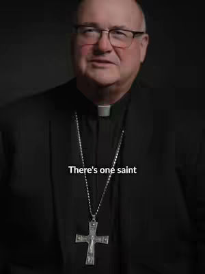 A medium shot features a man in a suit and clerical collar, wearing glasses. A silver cross hangs from his neck, and text overlays at the bottom.