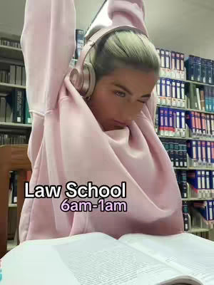 A young woman in a pink hoodie sits in a library, resting her arms up as if stretching. The cover image shows a book on the table with text overlayed.
Behind her are library shelves full of books organized by color and title. Text overlays at center bottom read "Law School" and "6am-1am".