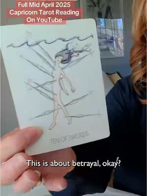 A hand holds up a tarot card with an illustration of a figure with blades. The image has text overlaid in the top left and bottom of the card.