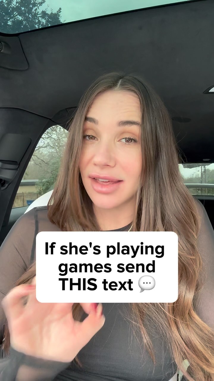 A woman with long brown hair is sitting in a car. The woman is looking at the camera. Overlaid on the image, within a white rectangle, is the text: "If she's playing games send THIS text".