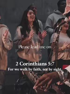 A group of people, likely a choir or worship team, are singing and playing instruments on a stage. In the foreground, a woman with long dark hair is singing with her hands clasped in front of her. The background is dark, with other people visible. Text overlays the image.