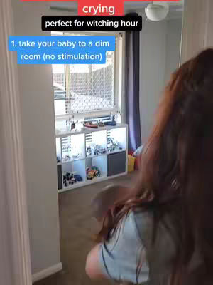 A person, seen from the back, holds a baby while walking into a dim room. Text overlays provide instructions on how to stop a baby from crying.