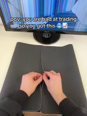 The cover image shows a person's hands in the foreground, holding a white cord or string stretched between two black surfaces, presumably a desk mat. Behind the hands is a monitor with a cracked and broken screen. The text overlay on the screen says, "pov: you are bad at trading so you got this." Additional elements include a small keyboard and a dark surface. The image uses a muted color palette and a straightforward composition.