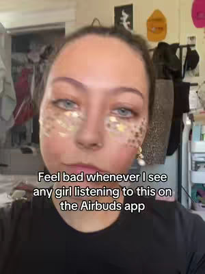 A selfie-style shot focuses on a young woman's face against a blurred background. She has light skin, and her face is adorned with what appears to be glitter or sparkles around her eyes. The text overlayed on the image reads, "Feel bad whenever I see any girl listening to this on the Airbuds app."