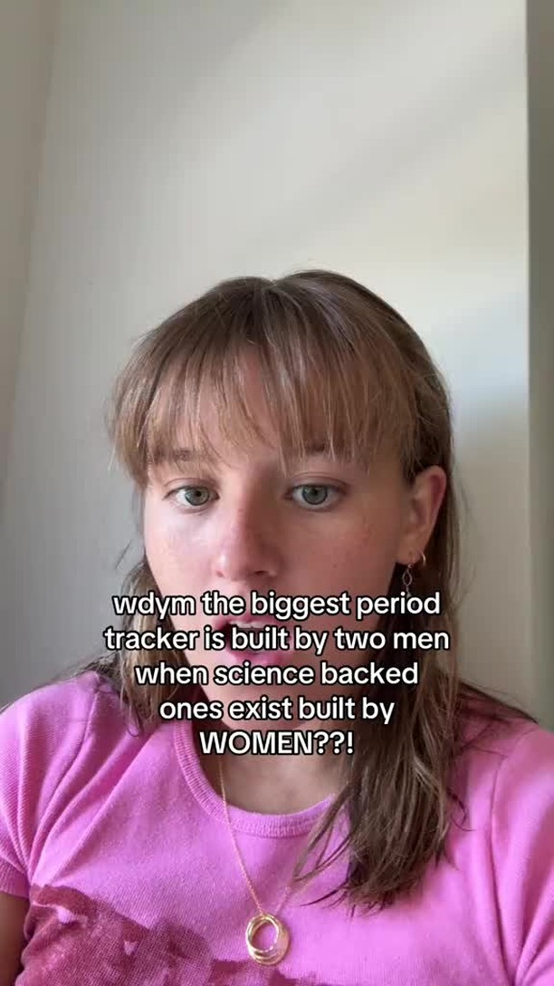 A close-up of a young woman with light skin and shoulder-length blond hair looking directly at the camera. She is wearing a pink shirt and a gold necklace. Text overlaid on the image poses a question about period tracking apps.