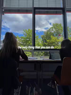 Two people, partially visible from the back, are studying at a desk by a large window overlooking a bright, cloudy sky and green trees outside. Text overlayed says, 'the only thing that you can do'.