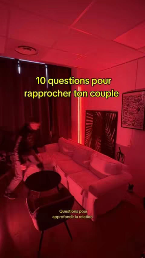 A room with a white settee, a black table, and a person walking. The room is lit in a red hue.
