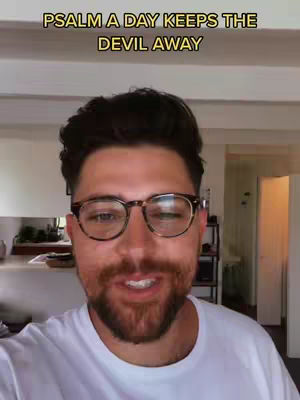 A man with a beard and glasses is centered in the frame, with text above his head. The background is blurred, hinting at an indoor setting.