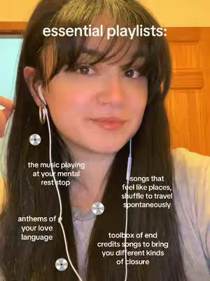 A woman with long dark hair and bangs looks directly at the camera. She wears earbuds and appears to be in a home setting with wooden trim visible in the background. White text and small silver circles are added as overlays, pointing to the text and giving the video context.