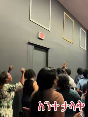 A group of people are gathered in a room with dark gray walls. The people are facing away from the camera, some with their hands raised. The hook is written in red text. Above the people are picture frames.