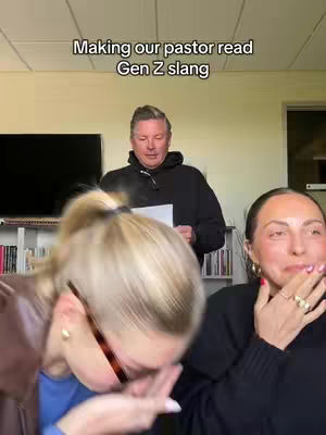 The cover image shows three people in an interior setting. In the foreground, a woman with blonde hair pulled back in a ponytail leans forward, appearing to laugh or be startled, her face partially obscured by her hand. To her right, another woman with dark hair and large gold hoop earrings reacts with a similar expression, seemingly covering her mouth. In the background, a man in a black hoodie stands, holding a paper. The background is a neutral-colored wall and includes a shelf of books. The text overlay at the top says, "Making our pastor read Gen Z slang".