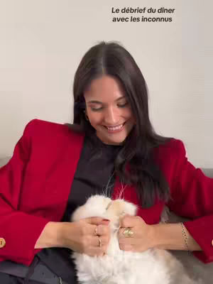 A smiling woman in a red blazer holds a white fluffy cat close to her chest. The photo is composed with the woman's face and the cat filling most of the frame.
