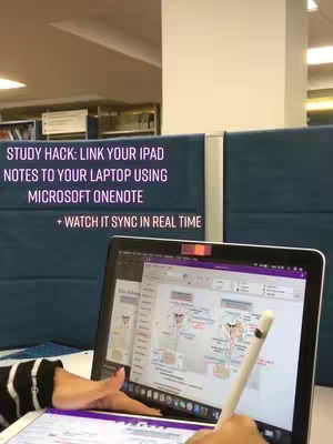 A person is working on a laptop and an ipad in front of a blue cubicle wall. On the laptop screen, there is an image of a chart and a digital pen in their hand. The ipad is in front of the laptop.