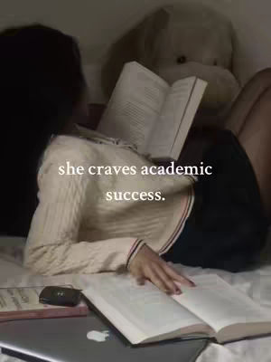 A woman is lying in bed, reading a book. The image is softly lit, suggesting a calm and focused environment. Text overlayed on the image reads, "she craves academic success."