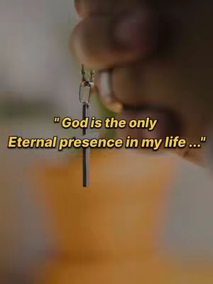 The cover image is a close-up shot focusing on a hand holding a silver cross pendant. The cross is the central element, positioned vertically against a softly blurred background. The hand is slightly out of focus, drawing more attention to the cross. Overlay text in a yellow color is positioned on the lower center of the image. The background has a blurred warm gradient and suggests an indoor setting with soft lighting.