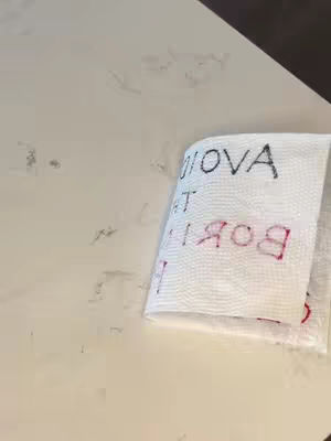 The cover image shows a piece of folded white paper on a light-colored surface. The paper has text written on it with black and red markers, though the text is presented in a way that it is partially obscured by the folds.