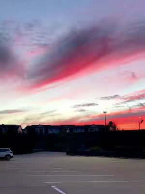 The cover image features a vibrant skyscape at dusk. The sky is filled with dynamic streaks and clusters of pink, red, and purple hues, suggesting a sunset or sunrise. Below the sky, a dark silhouette of buildings and a parking lot are visible, with a car parked in the foreground, adding depth and context to the scene, giving a feel a peaceful and contemplative atmosphere.