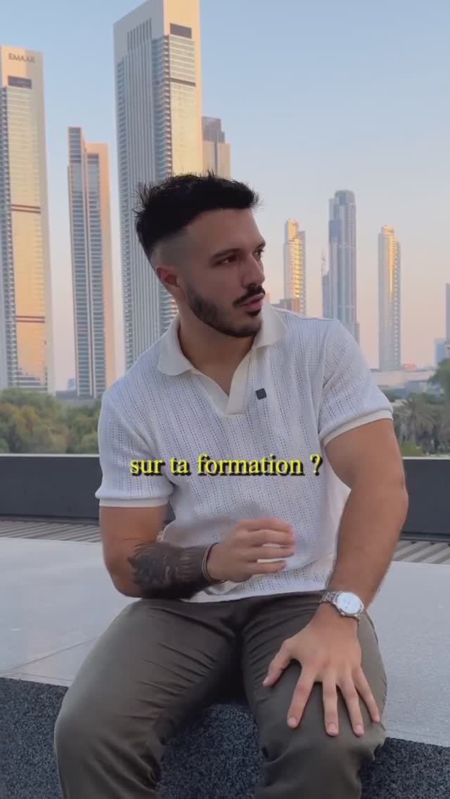 A man in a white polo shirt sits on a ledge with a cityscape of modern skyscrapers in the background. The foreground is a concrete surface. Overlaid on the image is text in yellow.