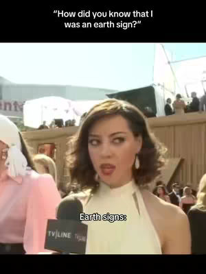The cover image features a woman in a yellow dress in front of what appears to be a red carpet background. She looks at the camera with a surprised expression; text overlay indicates the video content is about earth signs.