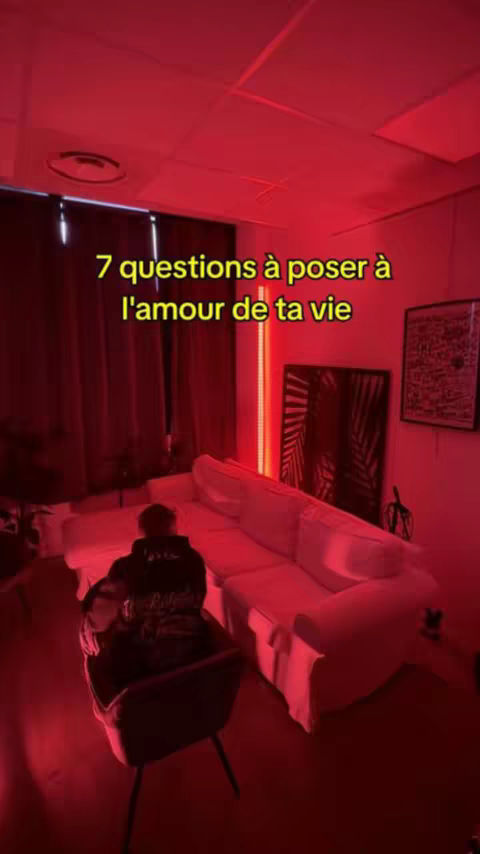 The image is a dimly lit room bathed in a warm, red glow. A person is seated in a chair, their back towards the camera, with a hoodie. A white couch is prominently positioned, suggesting a domestic setting. The text overlay provides context about the video's content.