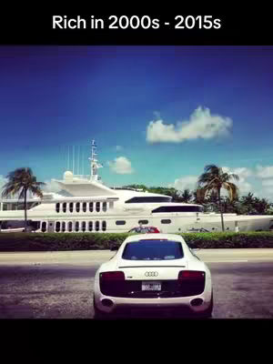The cover image showcases a luxurious scene with a white sports car parked in front of a large white yacht, suggesting a lifestyle of wealth and leisure. The backdrop includes a lush green barrier and palm trees against a bright blue sky, creating a sunny, upscale atmosphere. The composition emphasizes the opulence associated with the location.