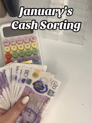 The image shows a hand holding a stack of banknotes, with a calculator and a clear plastic container on a white surface. The text overlay at the top says 'January's Cash Sorting'. The composition suggests a focus on budgeting or financial organization.