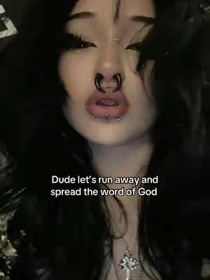 Close-up shot of a young woman with dark hair and multiple piercings. She has dark eye makeup and full lips. A text overlay reads, 'Dude let's run away and spread the word of God.