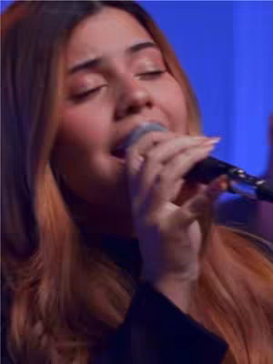 The cover image shows a close-up of a woman singing into a microphone. She has long, light brown hair, and her eyes are closed, suggesting she is deeply engaged in the performance. She is wearing a black top. The background is a blurry blue.