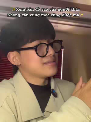 A person wearing glasses and a black cap is captured in a medium shot from the chest up, set against an indistinct background, possibly an interior. The individual is speaking, and a microphone is attached to their clothing, suggesting they are either recording or broadcasting. The lighting is soft, and the overall composition is simple, focusing on the subject's expression and gestures.