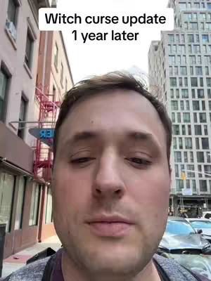 A man stands in a city street, facing the camera with buildings and a sign in the background. The upper part of the image has white text overlay.