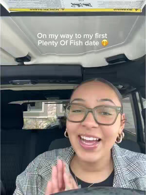 A woman with glasses smiles widely while looking towards the camera. She's seated in a car, visible through the windshield and part of the car's frame. The background includes houses and the interior of the car. The overall image has a candid, friendly feel. Overlaid text says 'On my way to my first Plenty Of Fish date'.