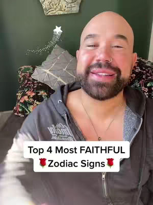 A man with a bald head and a short beard is smiling at the camera. He is wearing a gray hoodie and a necklace. There are pillows and decorations in the background. Text on the image says: "Top 4 Most FAITHFUL Zodiac Signs".
