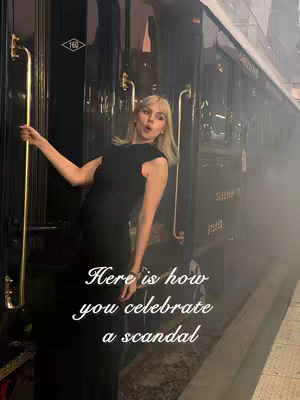 A woman in a black dress leans against a train car door, posed in a playful manner. Text overlayed on the image reads "Here is how you celebrate a scandal."