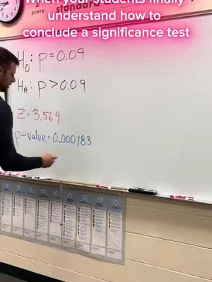 A man is standing next to a whiteboard, writing mathematical equations. The whiteboard is filled with equations related to significance tests, with formulas and numerical values. The man stands turned towards the board and holding a pen.