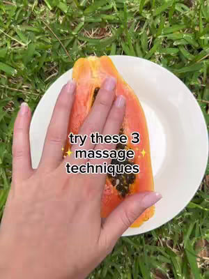 A close-up shot shows a hand reaching toward and partially covering a slice of papaya, with some added text in the image, set against a backdrop of green grass and a white plate. The papaya slice is in the front, showing its orange-red flesh with black seeds.