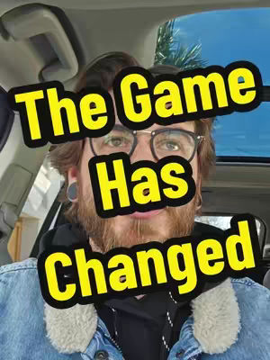 A man with a beard and glasses is centered in the frame. He is in a vehicle. The text overlay reading "The Game Has Changed" in a yellow font is placed over the man's face. The background includes parts of the car's interior and a glimpse of a bright sky.