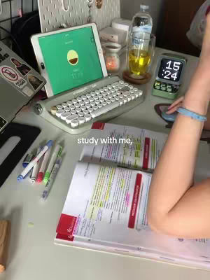 A desk with a laptop, tablet, and books, with a person's arm in the frame.