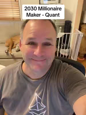A middle-aged man smiles directly at the camera, framed in a selfie. The background includes a couch with a dog resting on it, blinds, and a baby gate.