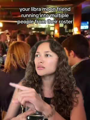 A woman with curly brown hair is pointing to her right with a serious expression, in a crowded bar setting. Text overlayed reads 'your libra moon friend running into multiple people from their roster'.