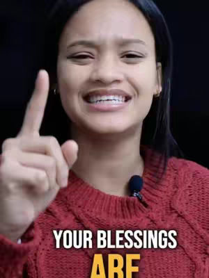 A woman with dark hair and a red sweater points her index finger upward. Text overlayed at the bottom reads 'YOUR BLESSINGS ARE' in bold font.