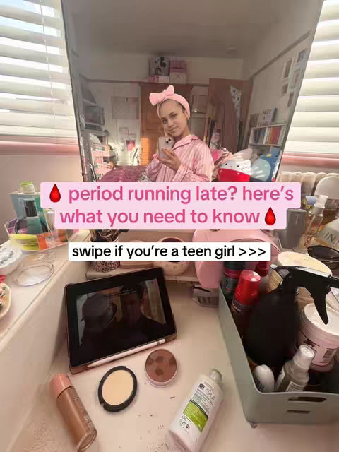 A young woman is reflected in a mirror, holding her phone up to take a photo. The mirror is surrounded by makeup items on the vanity. Text overlays with pink backgrounds are added to the image. There is also a reflection of what she is filming on her phone.