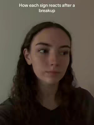 A selfie-style shot featuring a young woman looking slightly off-camera with a neutral expression. The background is a plain, light-colored wall. The top of the frame contains the text overlay: "How each sign reacts after a breakup".