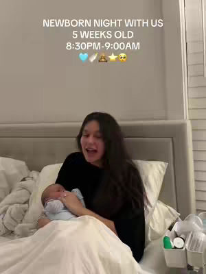 A woman holding a newborn baby in bed. Text overlay at the top of the frame describes the setting. The room has neutral tones with white bedding.