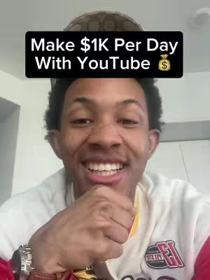 A man is smiling widely at the camera, with overlaid text in a black box above his head. He wears a white and red jacket and a watch. Behind him is a neutral background.