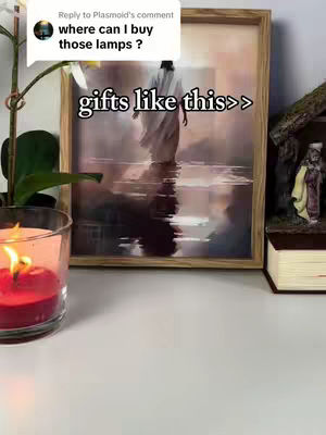 The image features a framed artwork of Jesus walking on water, displayed on a white surface. In front of the artwork, a red candle burns inside a glass, and near the background, there is a nativity scene figurine on a book. The background is intentionally blurred, however, a comment asking where to buy the items is overlaid on the image.