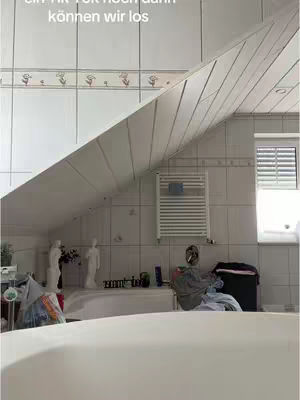 The cover image shows a bathroom scene. A woman sits on the edge of a large white bathtub. Above, a sloped ceiling transitions from white tiles to a slanted paneled ceiling, partially obscuring the upper area. The walls are lined with white tiles with a floral border. The room includes a window with blinds, a towel rack, and some decorative items. The lighting is natural, creating a bright atmosphere.