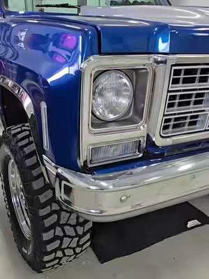 The cover image features a close-up of a blue classic truck, emphasizing its front right side. The truck's blue glossy surface reflects light, and details like the front tire, headlight, bumper, and chrome accents are visible. The vehicle is parked on a smooth surface, and the composition is well-lit, showcasing the truck's design.